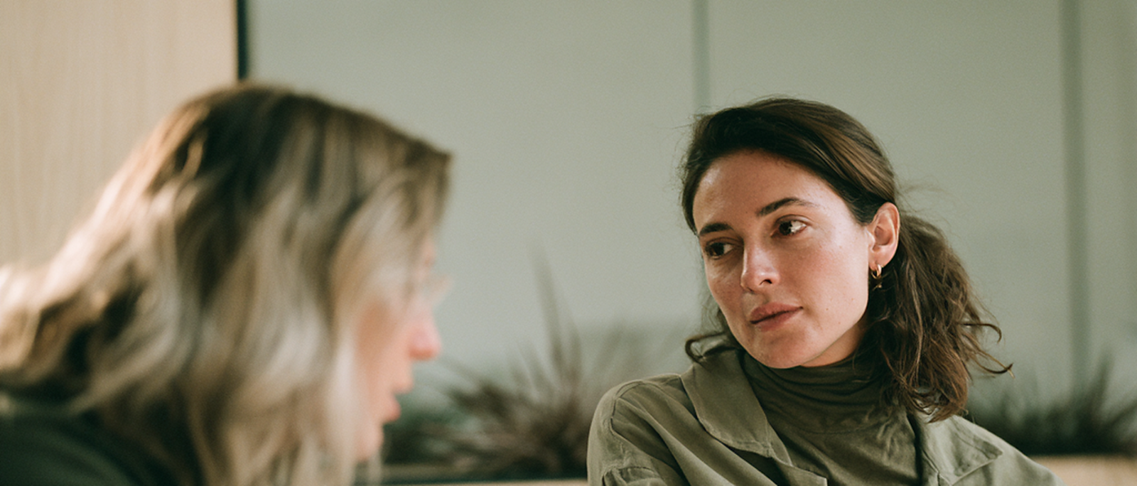 Two buyers at a table weighing one option against another, one listening with a considering, unconvinced expression.